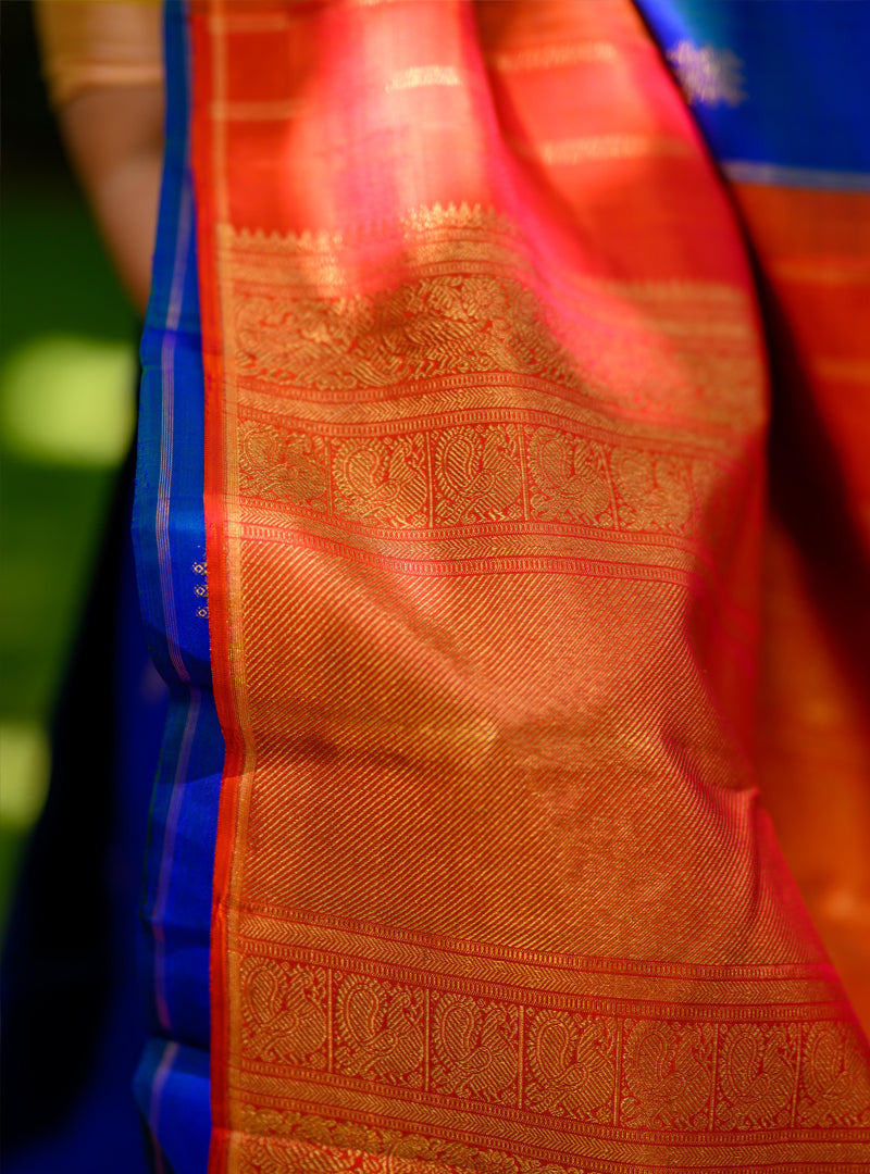 A borderless kolam butta kanchivaram in shot color peacock blue and rust orange.