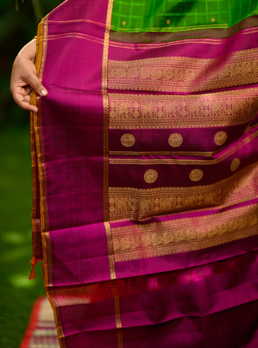Pure silk, pure zari semi-contrast Ganga Jamuna Kanchivaram featuring a beautiful parrot green kattam on a leaf green body, with delicate floral buttas woven within the checks.