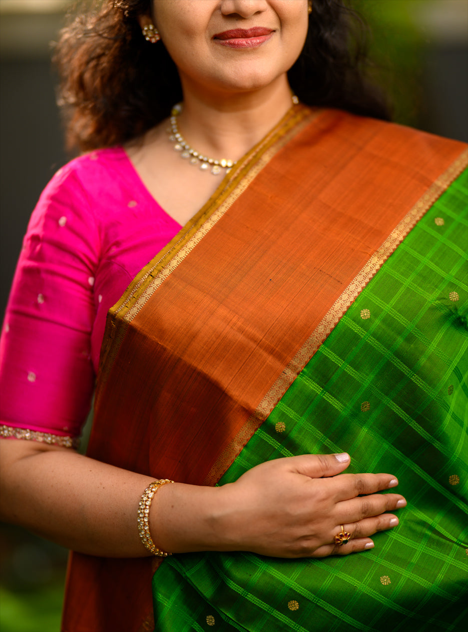 Pure silk, pure zari semi-contrast Ganga Jamuna Kanchivaram featuring a beautiful parrot green kattam on a leaf green body, with delicate floral buttas woven within the checks.