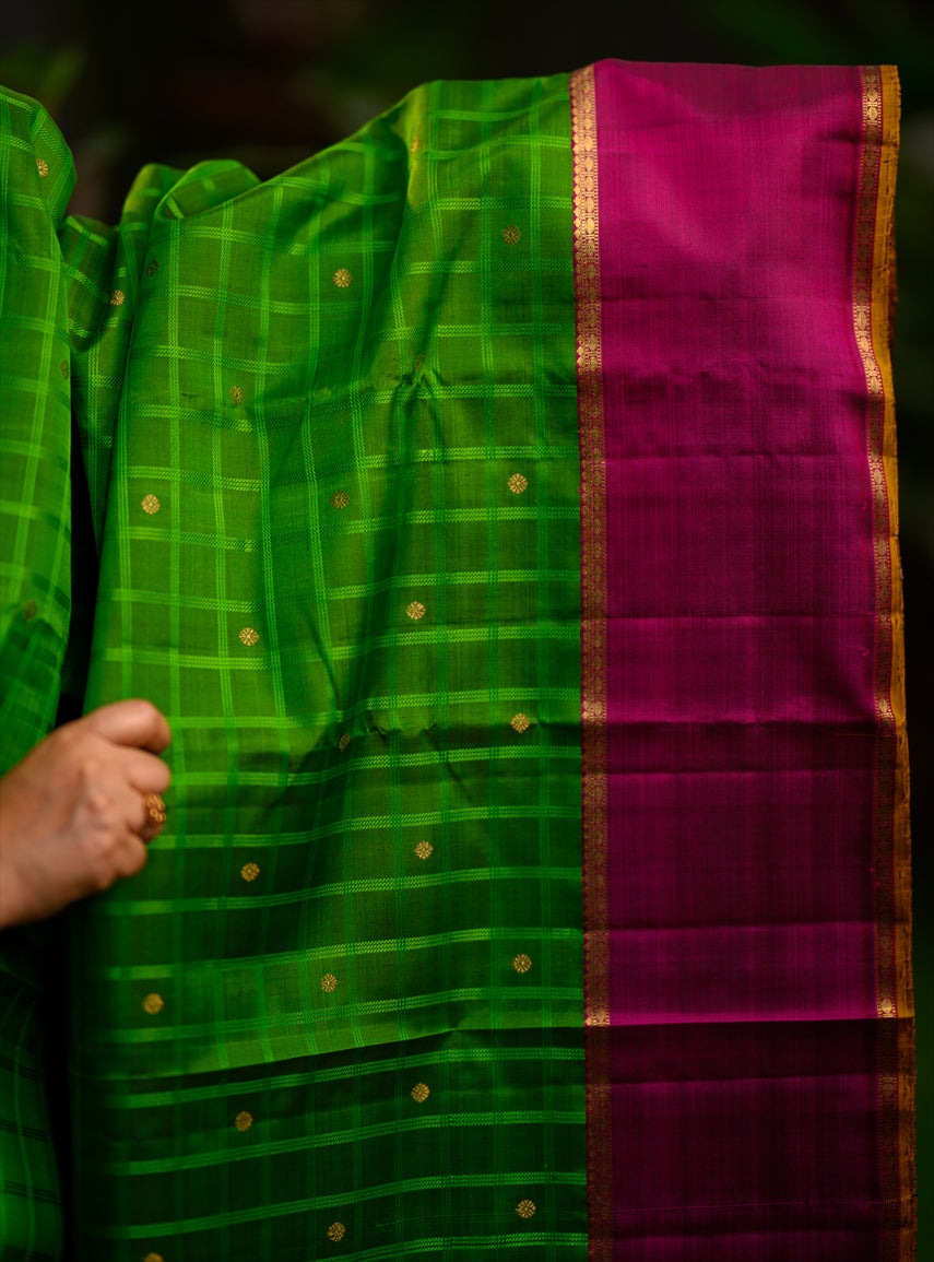 Pure silk, pure zari semi-contrast Ganga Jamuna Kanchivaram featuring a beautiful parrot green kattam on a leaf green body, with delicate floral buttas woven within the checks.